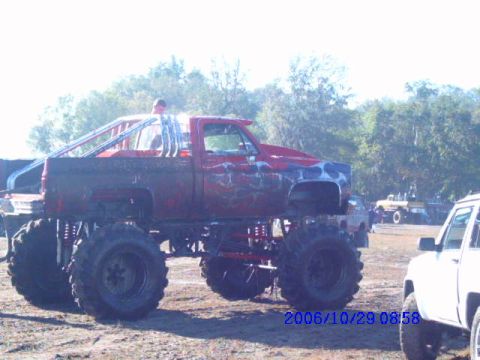 1987 Suzuki Samurai - A heavily modified red truck with oversized tires and a roll cage is shown in an outdoor setting.
