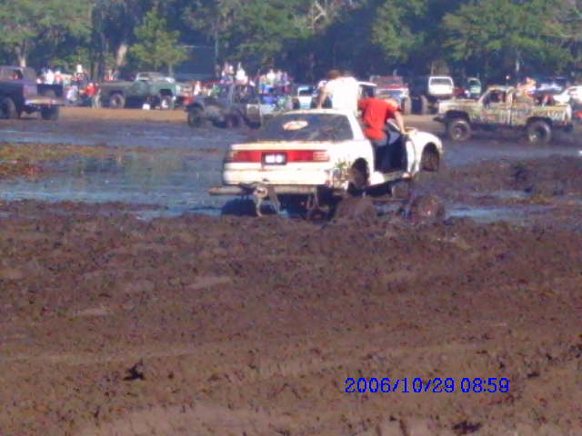 White SUV with red stripe stuck in mud, rear view