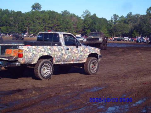 1987 Suzuki Samurai - Muddy field event with multiple trucks and spectators present.