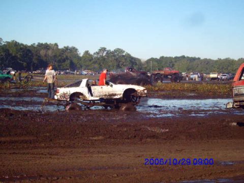 1987 Suzuki Samurai - Vehicles are stuck in a muddy field during an event, with spectators and other vehicles in the background.