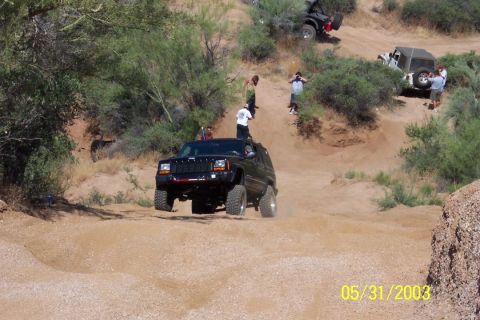 1993 Ford Bronco - Multiple off-road vehicles navigate a dusty trail with onlookers.