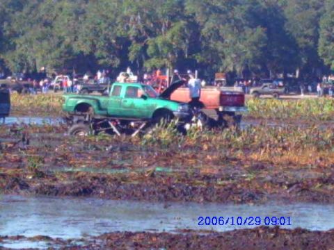 1987 Suzuki Samurai - A lifted pickup truck is stuck in the mud with a trailer attached. Multiple vehicles and spectators are visible.