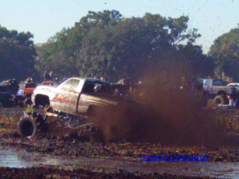 1987 Suzuki Samurai - A heavily modified pickup truck navigates a muddy terrain, kicking up a large spray of dirt.
