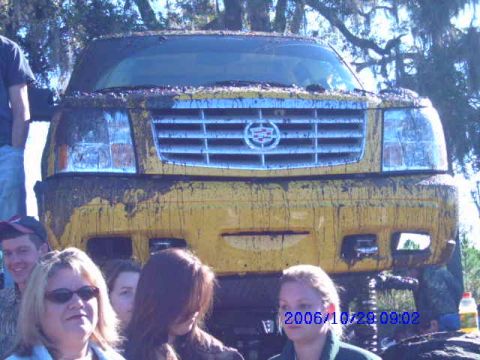 1987 Suzuki Samurai - A yellow SUV, heavily coated in mud, is shown from the front, displaying its grille and headlights.