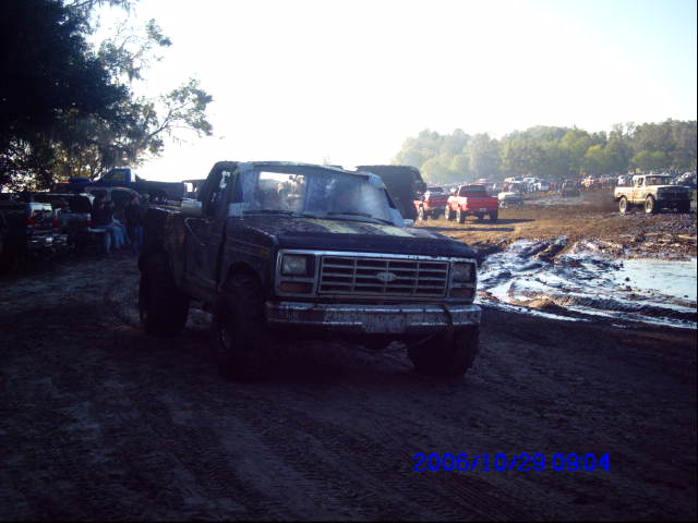 Muddy pickup truck in a mud pit with other trucks in the background
