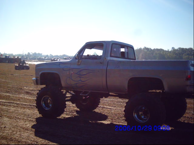 Lifted pickup truck with blue flame decals on the side, parked in a dirt lot