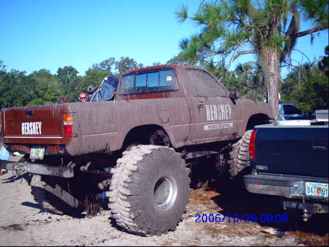 Muddy pickup truck with huge tires, "HERSHEY" on tailgate and side. Another truck is next to it