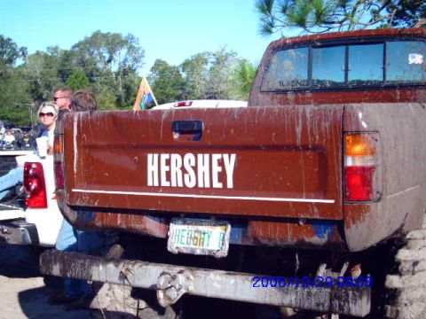 1987 Suzuki Samurai - A brown pickup truck with "HERSHEY" on its tailgate is seen from the rear, covered in mud.