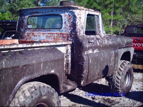 1987 Suzuki Samurai - Mud-caked pickup truck in a wooded area, with another vehicle visible behind it.