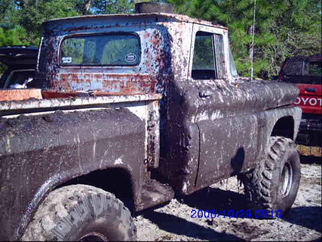 Mud-covered pickup truck with a red Toyota truck behind it