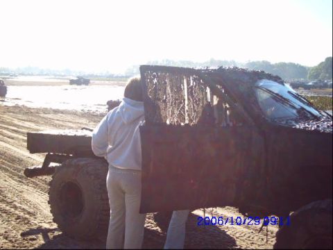 1987 Suzuki Samurai - A heavily mud-caked truck sits in a muddy, outdoor environment with two individuals near its open door.
