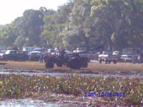 1987 Suzuki Samurai - An off-road vehicle with a crane arm is parked in a muddy area with other vehicles in the background.