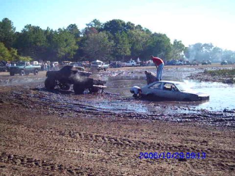1987 Suzuki Samurai - Multiple vehicles are stuck in the mud during an event, with spectators in the background.