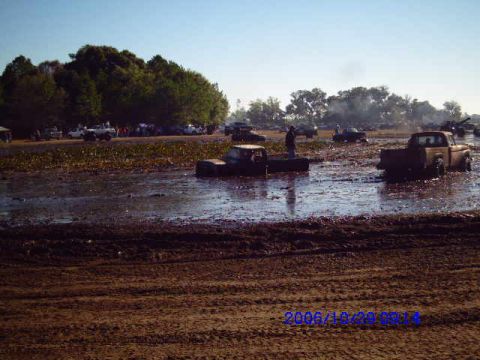 1987 Suzuki Samurai - Several trucks are stuck in a muddy area, with spectators gathered in the distance.