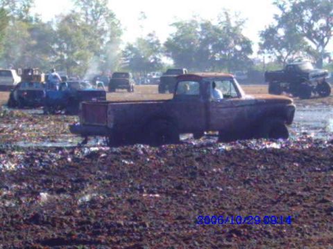 1987 Suzuki Samurai - A muddy pickup truck is stuck in a mud pit, with other vehicles visible in the background during an event.