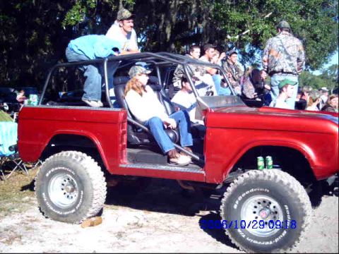 1987 Suzuki Samurai - A red off-road vehicle with a roll cage is parked outdoors with several people around it.