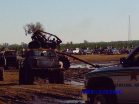 1987 Suzuki Samurai - Several off-road vehicles are gathered in a muddy field, with one truck carrying a roll cage structure.