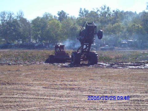 1987 Suzuki Samurai - A monster truck is shown performing a wheelie in a muddy area, with another vehicle visible in the background.