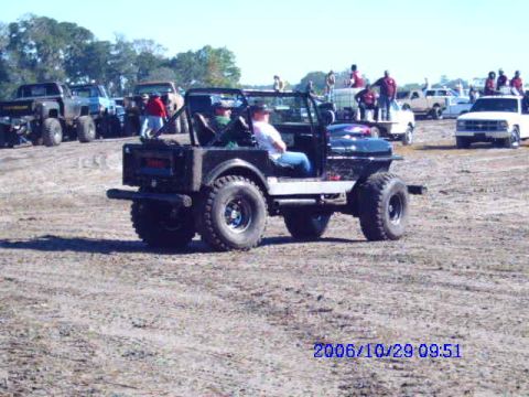 1987 Suzuki Samurai - A group of people are gathered around several off-road vehicles in an outdoor lot.