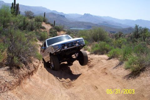 1993 Ford Bronco - A white Ford Bronco navigates a steep, dusty trail in a desert landscape.