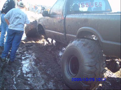 1987 Suzuki Samurai - Pickup truck with oversized tires stuck deep in mud, with 'ISSUES' visible on the rear window.