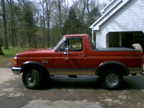 1989 Ford Bronco - This red Ford Bronco, likely from the late 1980s, is parked in front of a residential garage.