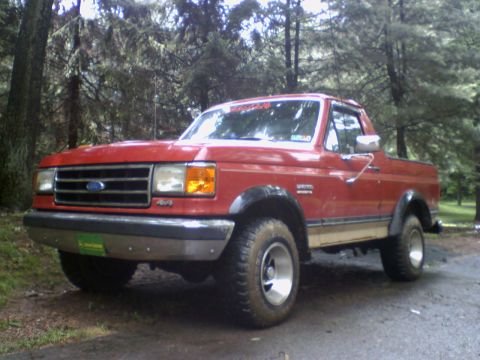1989 Ford Bronco - This 1989 Ford Bronco is shown in a wooded setting, off-road tires and a classic red exterior.
