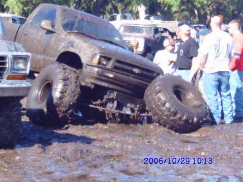 1987 Suzuki Samurai - A heavily mud-covered pickup truck is stuck in a muddy area with people observing.