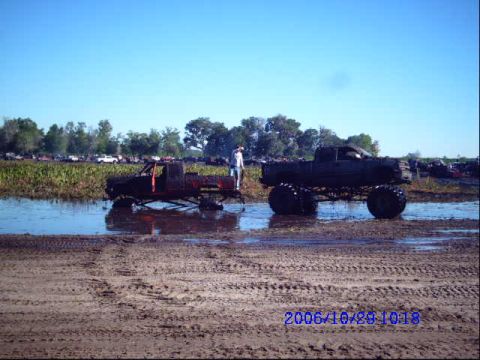 1987 Suzuki Samurai - Two heavily modified pickup trucks are stuck in the mud under a clear blue sky.