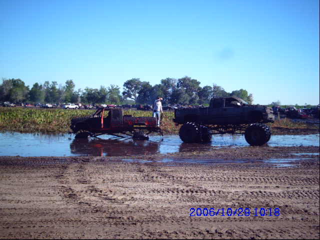 two lifted pickup trucks in a muddy field with a person standing between them
