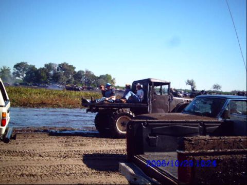 1987 Suzuki Samurai - Several vehicles are stuck in the mud and water under a clear blue sky.