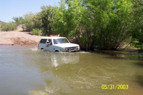 1993 Ford Bronco - White Ford Bronco driving through shallow water on a sunny day.