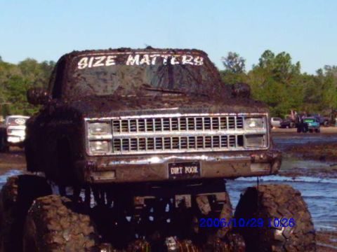 1987 Suzuki Samurai - This heavily mud-covered truck, likely from the mid-1980s, is seen in a muddy environment with other vehicles in the background.
