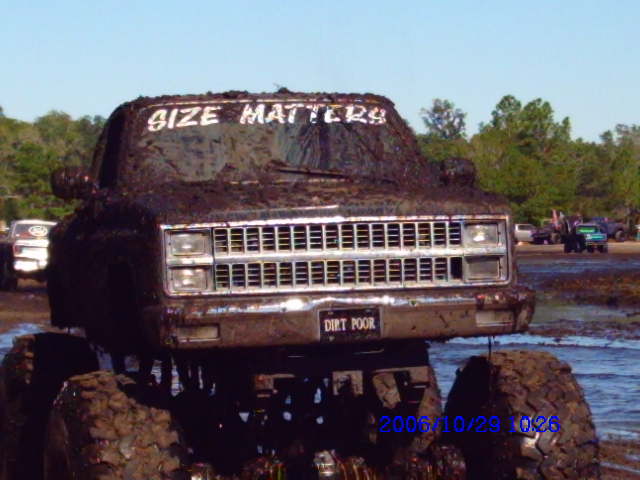 Mud-covered truck front view with "SIZE MATTERS" on windshield and "DIRT POOR" on license plate
