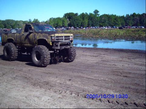 1987 Suzuki Samurai - Muddy lifted truck sits by the water, with other vehicles parked in the background.