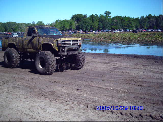 Mud-covered lifted pickup truck with large tires parked on dirt near water