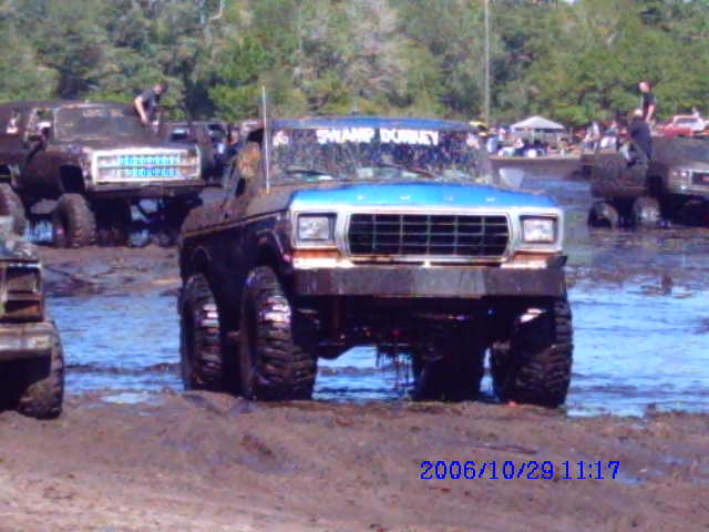modified pickup truck with blue top stuck in mud, other trucks and people around