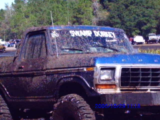 Mud-covered blue and dark truck, front 3/4 view, with 'SWAMP DONKEY' on windshield