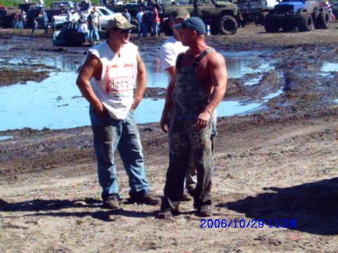 1987 Suzuki Samurai - Two men stand in a muddy area with several off-road vehicles visible in the background.