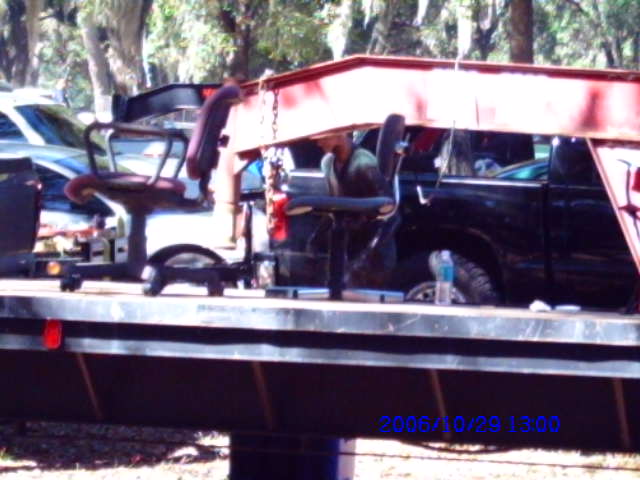 Two office chairs are loaded onto a flatbed trailer, with a black pickup truck partially visible behind them