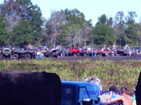 1987 Suzuki Samurai - A large group of off-road vehicles and people are gathered in a muddy outdoor area, with trees visible in the distance.