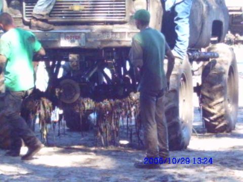 1987 Suzuki Samurai - A tractor with debris hanging from its underside is viewed from the rear, with two individuals standing nearby.