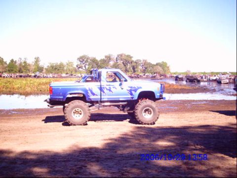 1987 Suzuki Samurai - Modified pickup truck sits in a muddy area with a body of water and trees in the background.