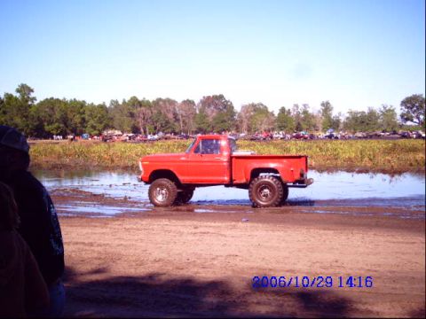 1987 Suzuki Samurai - A red pickup truck navigates a muddy terrain with other vehicles visible in the distance.