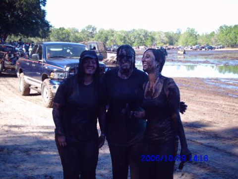 1987 Suzuki Samurai - Three women covered in mud stand in front of a blue pickup truck at a mud bog event.