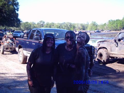 1987 Suzuki Samurai - Muddy participants pose for a photo at an off-road event with vehicles in the background.