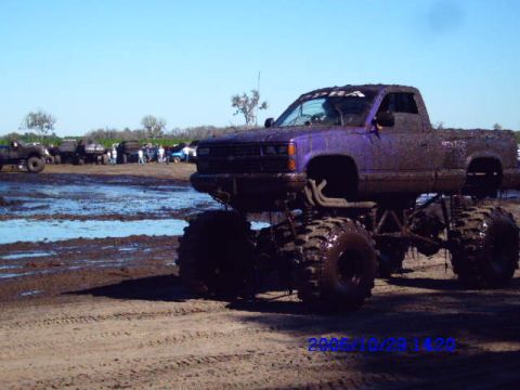 1987 Suzuki Samurai - A lifted pickup truck, caked in mud, sits in a muddy arena with other vehicles and spectators.