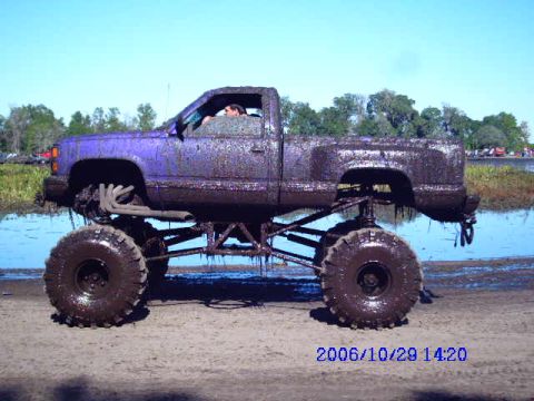 1987 Suzuki Samurai - Mud-covered pickup truck with lifted suspension and oversized tires seen in a muddy field.