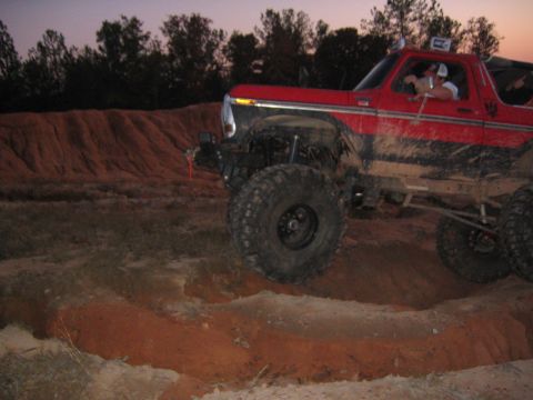 1979 Ford Bronco - A red off-road SUV navigates a dirt track at dusk.