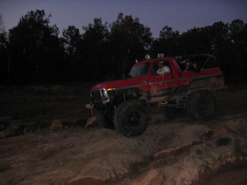 1979 Ford Bronco - This red 1979 Ford Bronco is navigating a rocky, uneven terrain as daylight fades.